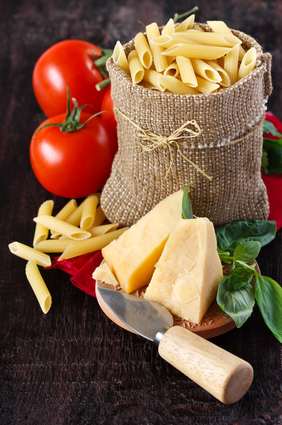 Ingredients for preparing pasta. Cheese, tomatoes, basil and pasta in a bag on a dark wooden background.