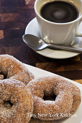 A plate piled high with donuts in front of a hot cup of coffee.